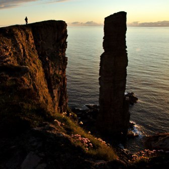 The Old man of Hoy sea stack with a person appearing on the skyline on the cliff opposite as the sun sets