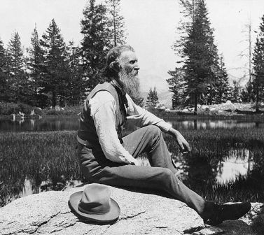 a picture of John Muir in older age resting on a big rock and looking towards the forest