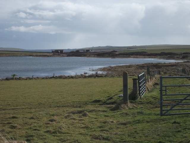 The loch of Tankerness stretches out in front with farming fields and fences in the foreground