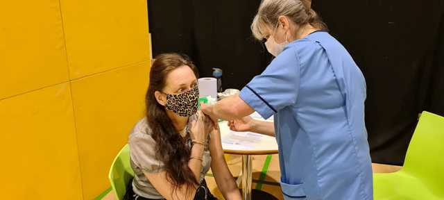 A woman being vaccinated by a health worker, both wearing masks
