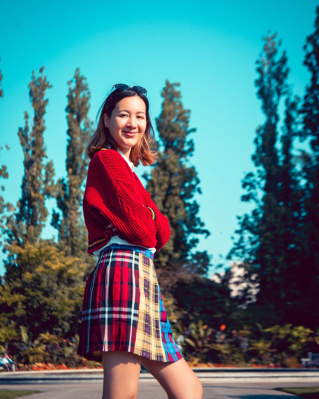 woman in red and blue plaid skirt and red crop top standing near green trees