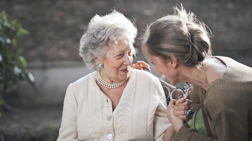 An older woman looking on at at younger woman - mother and daughter, who is supporting her and looking into each others faces