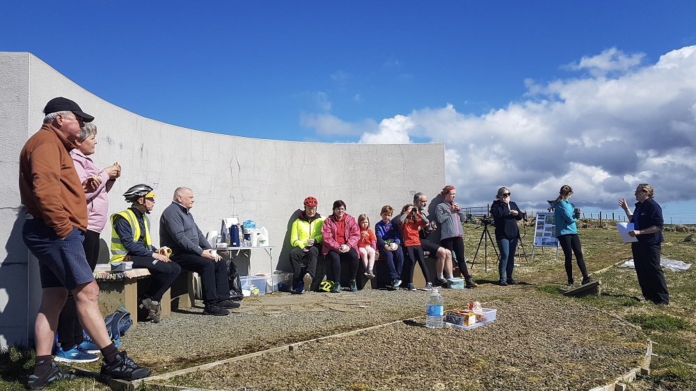 The family cyclists of all ages are sitting at the RSPB special listening curved wall at The Loons