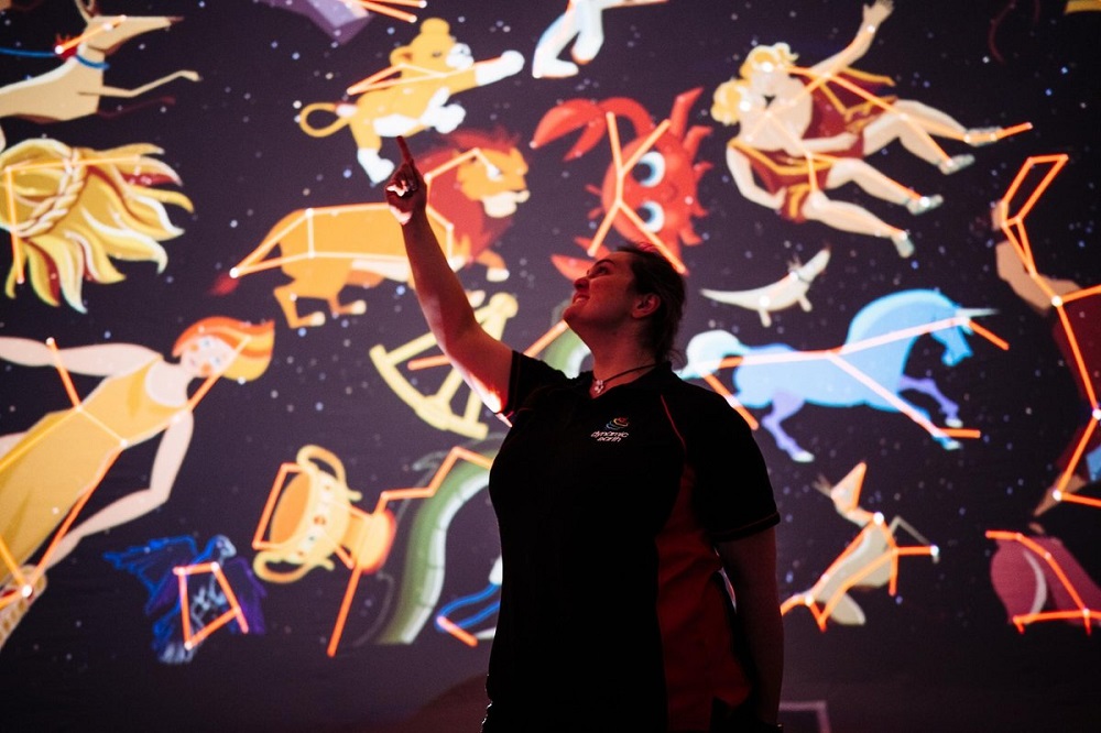 a woman pointing up at various mythological representations of the night sky and constellations