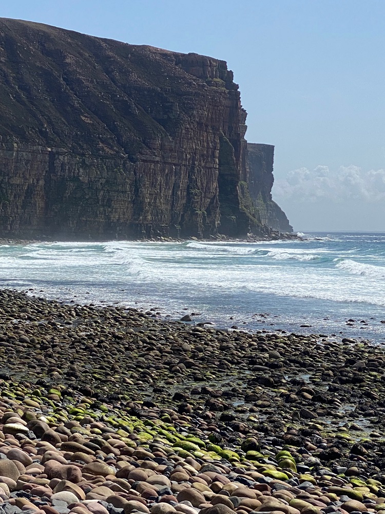 Standing on the pebble beach at Rackwick and looking towards the high cliffs and waves on the sea