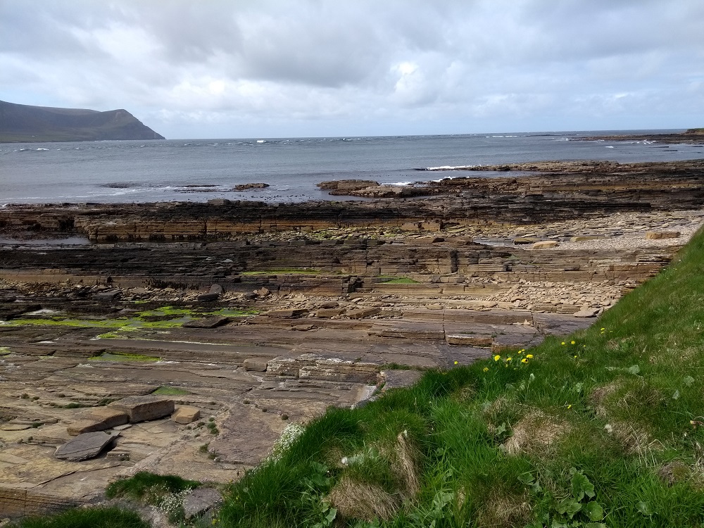the edge of Hoy can just be seen . The tide is very low and the rocks of the shoreline are exposed
