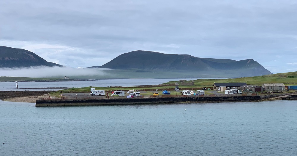 low mist lurks at the bas of the hills of Hoy and projecting out on the low headland is the camp site of Stromness