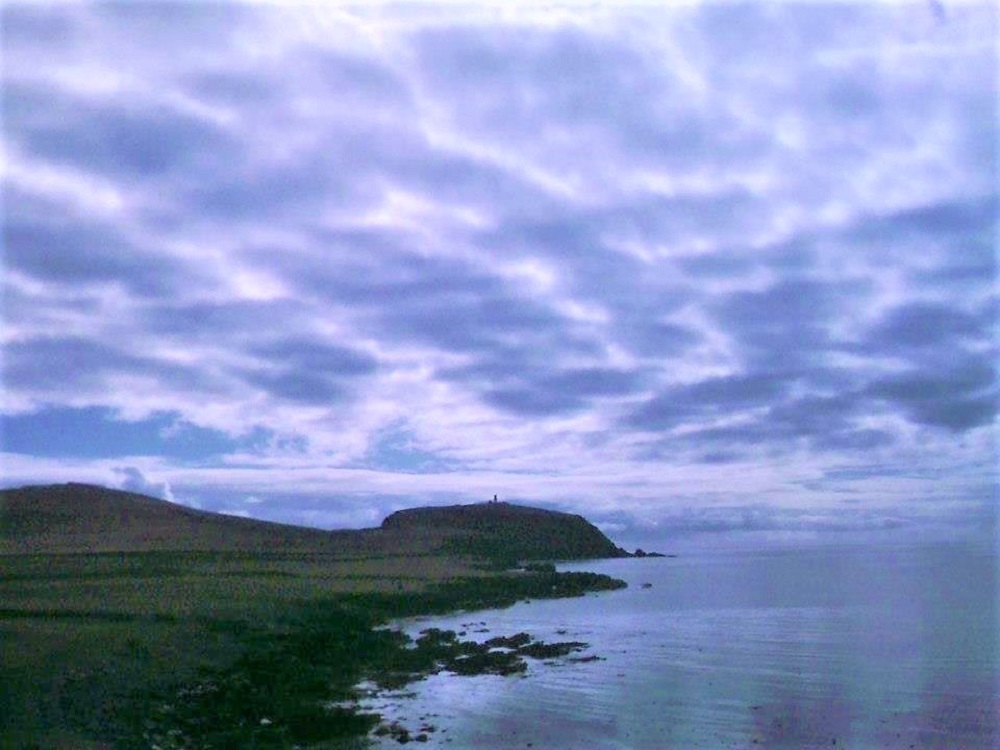 the rugged coastline at Virkie Shetland with the lighthouse in the distance