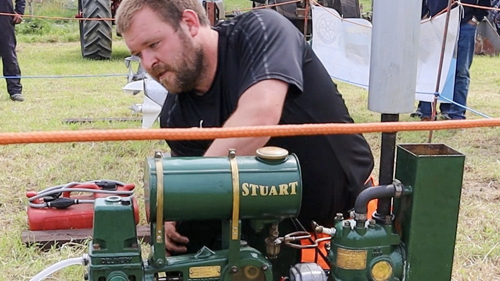 a man bends over a standing engine to adjust it