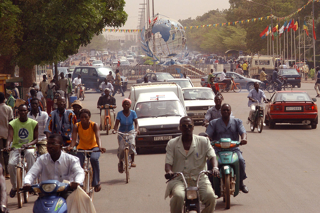 the busy street in Ouagadougou with lots of cars and people on bikes and motor bikes