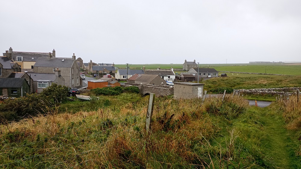from a grassy pathway the view over the bridge to the Palace village Birsay with its cluster of houses