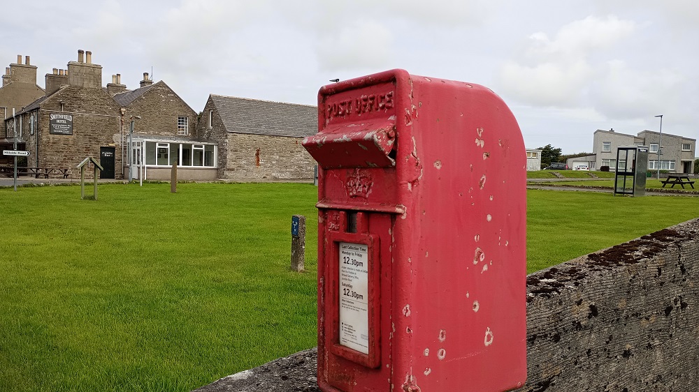 a rather battered looking post box on a stand near the Market Green Dounby