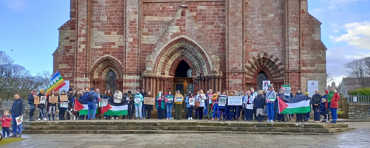 crowd of people on the steps of St Magnus Cathedral with Palestinian flags banners and Peace signs