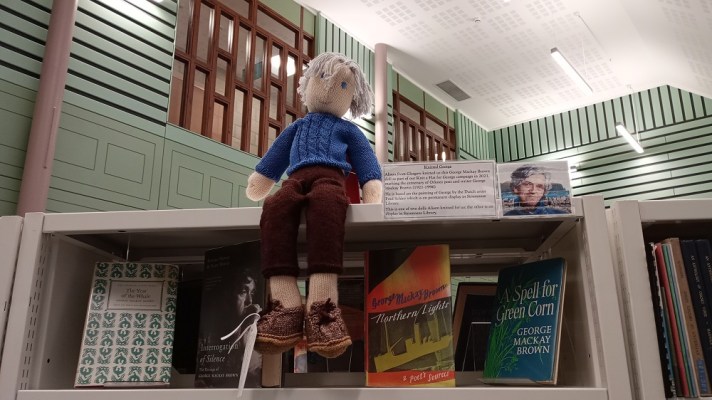 A knitted figure of George Mackay Brown sits on the top shelf of his books