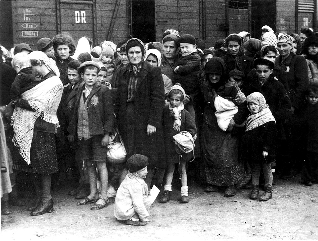 women children and men lined up with their few belongings waiting at the train to be transported for selection in the Nazi Concentration Camps
