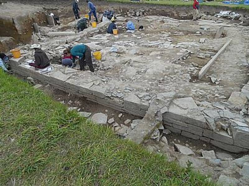 excavation showing people working on it and a long straight stone wall