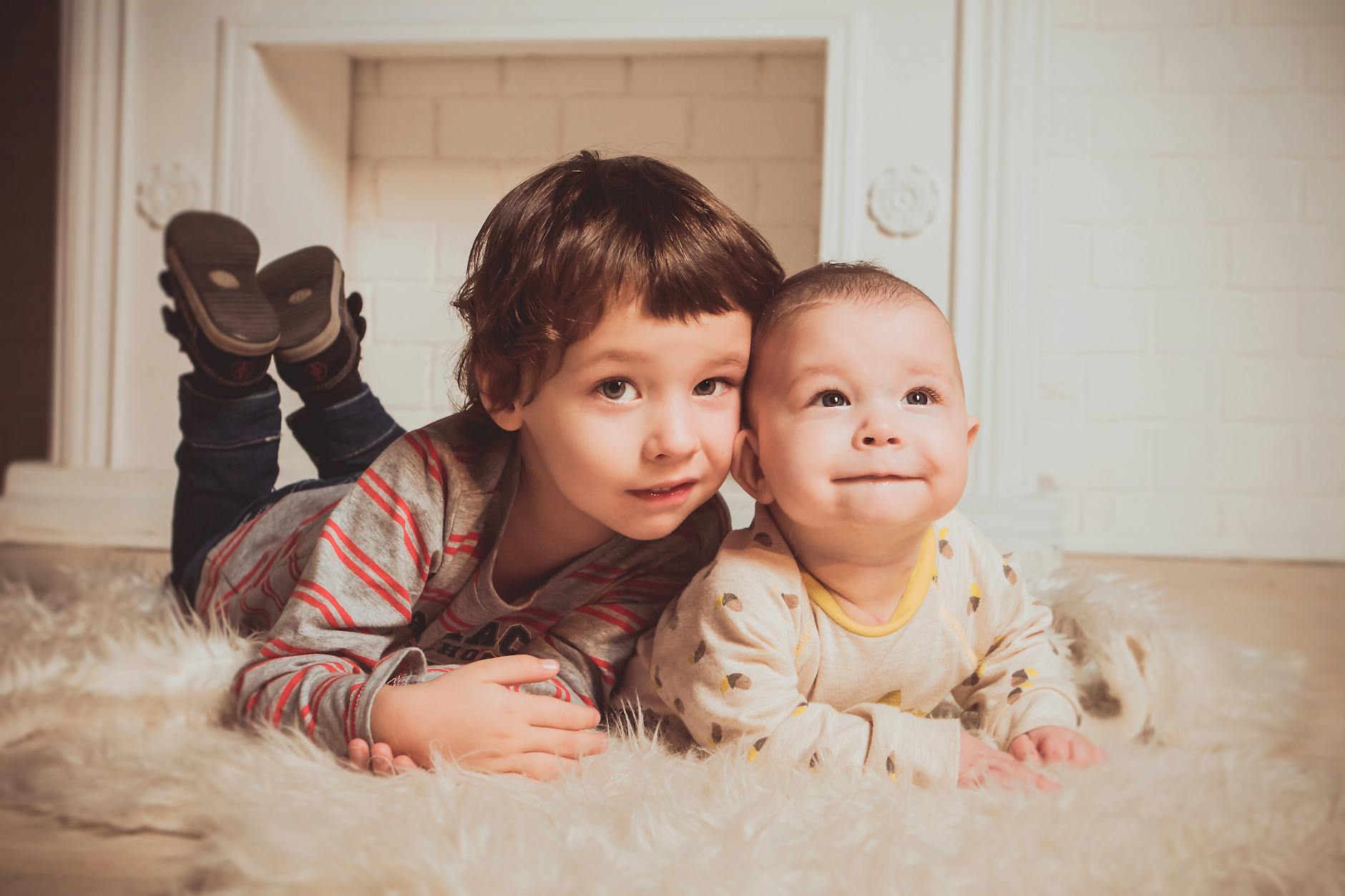 boy lying beside baby on mat