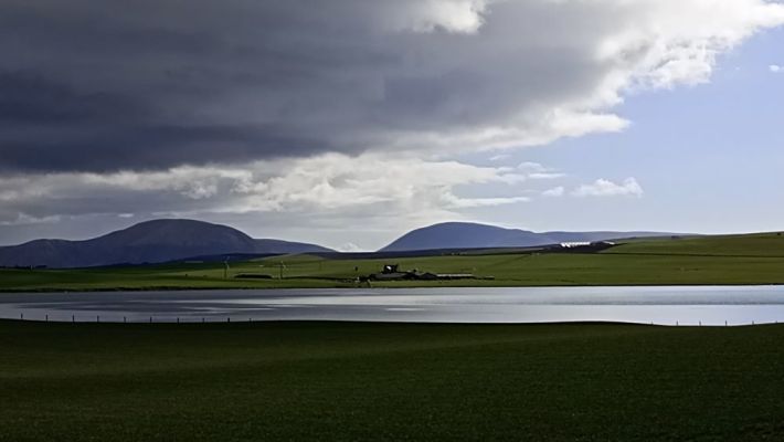 the hills of Hoy as seen from the low lands of Sandwick across the loch of Stenness with a cloudy sky