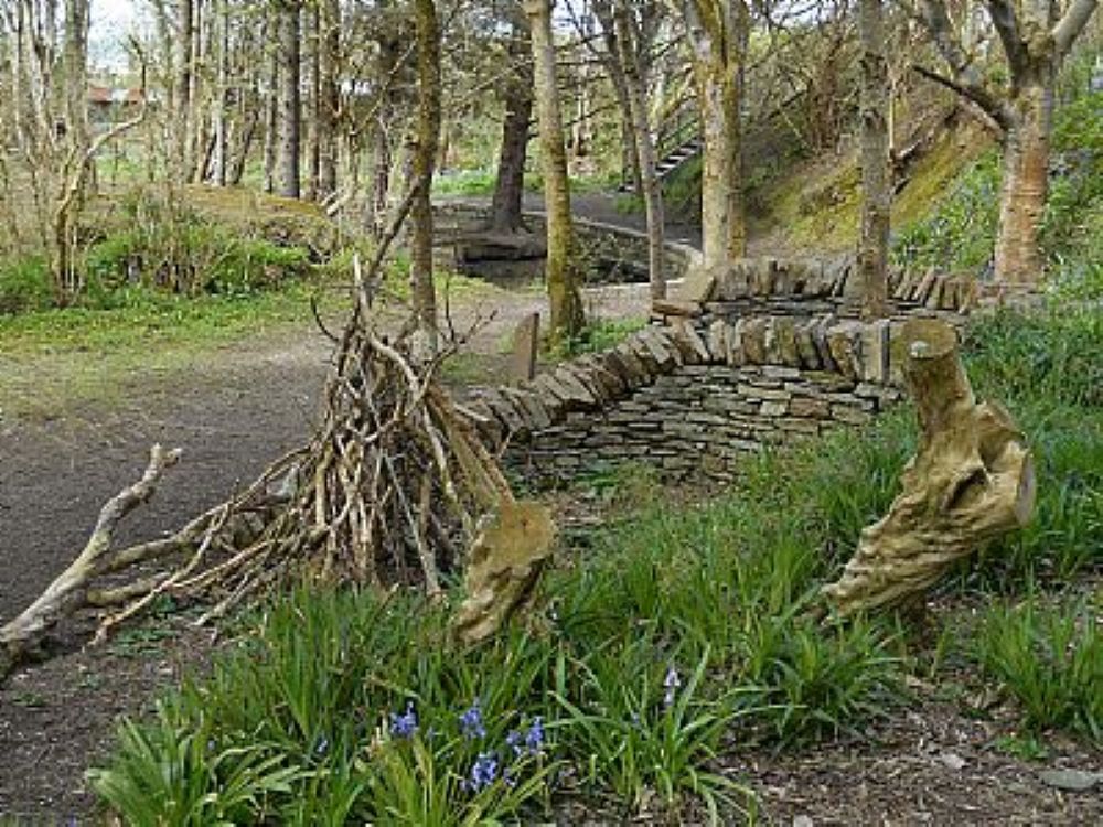 small pyramid shape of branches in the wood beside a stone seat