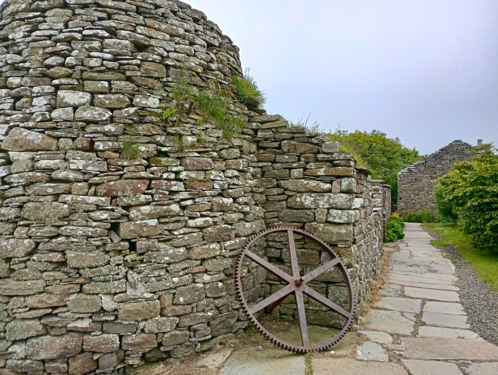 the path alongside the remains of the kiln and stable with a large cart wheel propped up beside it.