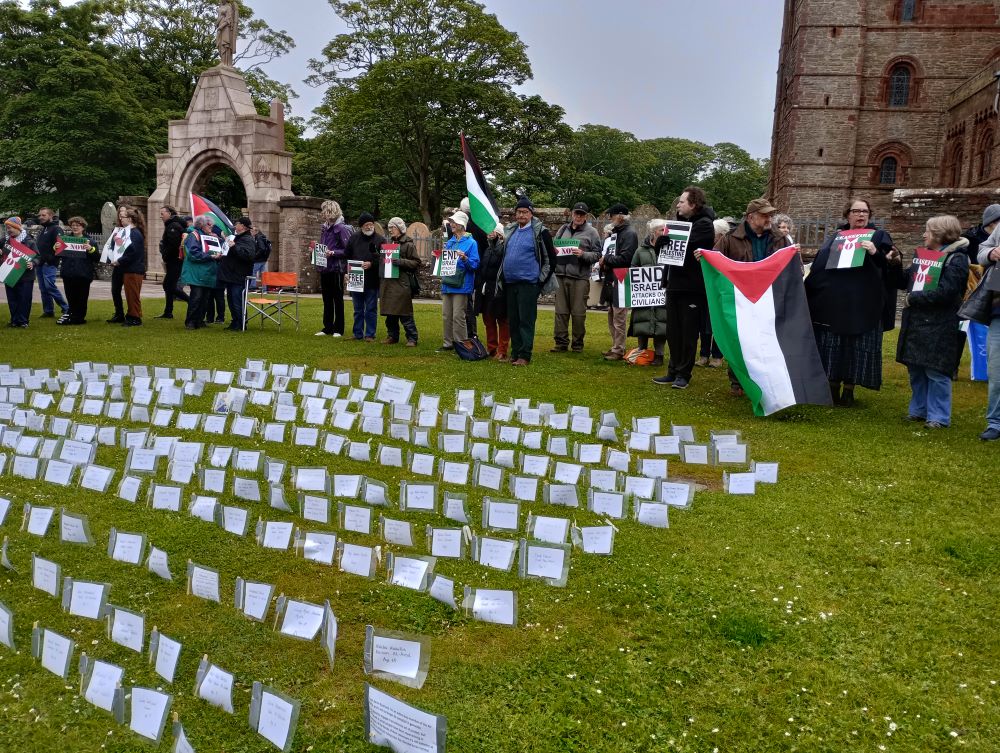 islanders standing with banners and flags in front of an array of names of those killed