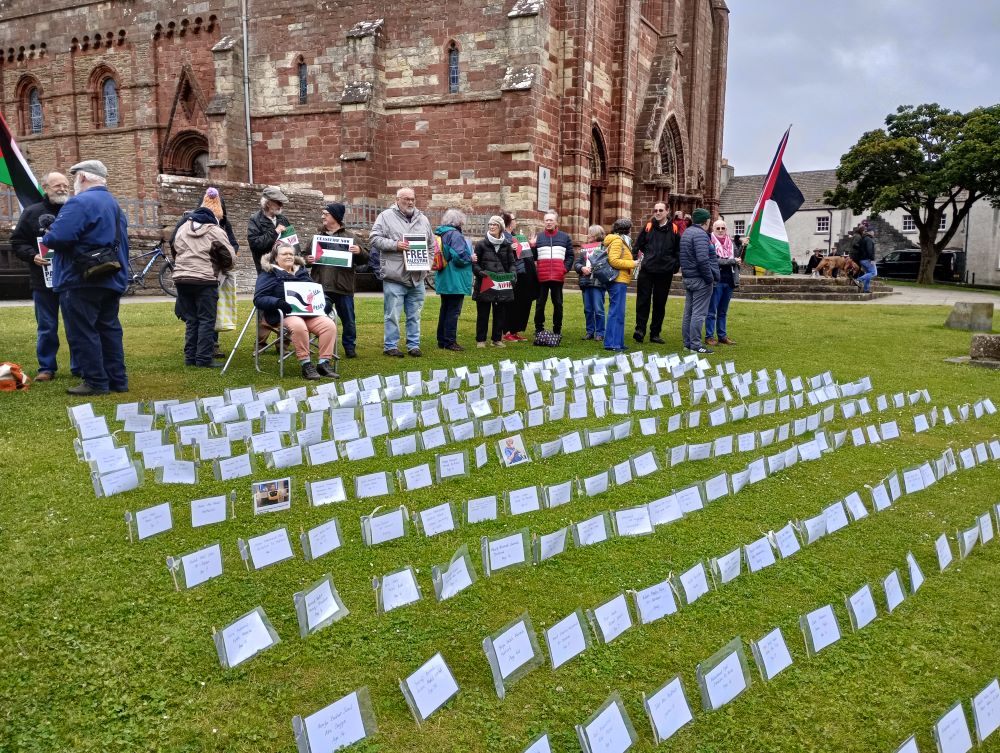 islanders on the kirk green standing beside the memorial names of some of those killed