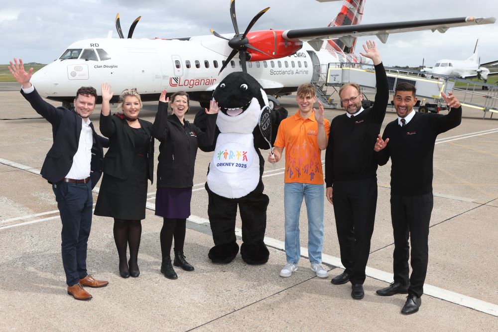 in the centre is the mascot of the islands games and behind the group a loganair plane