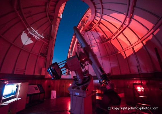 a man sitting looking through a giant telescope