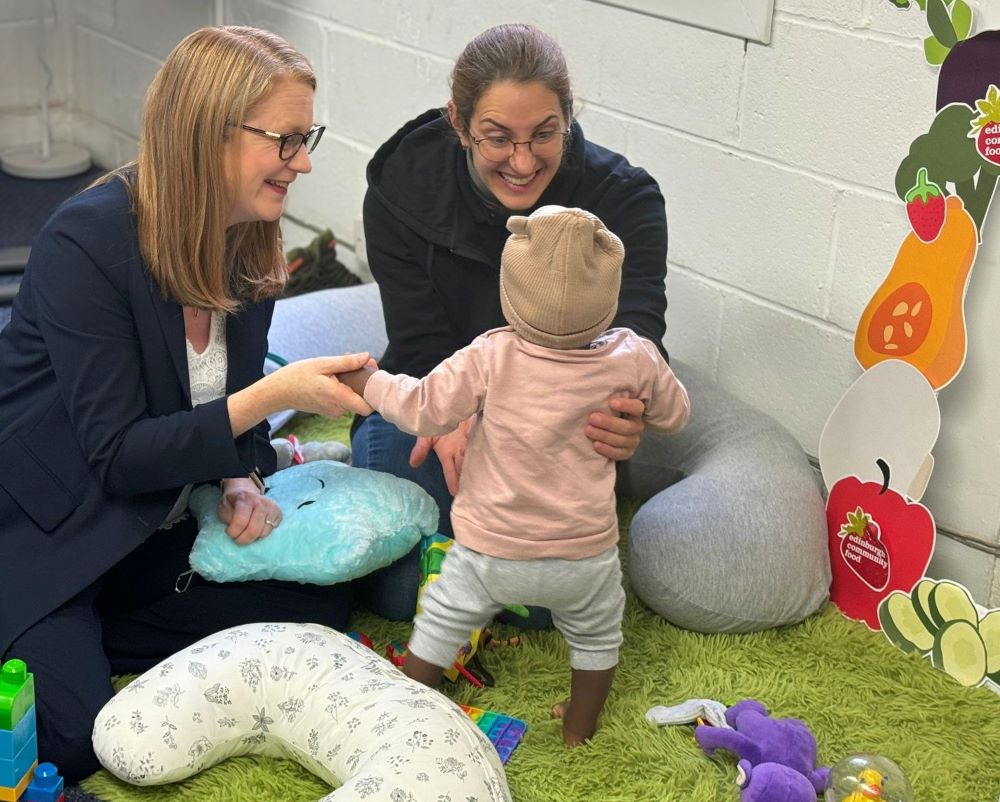 Shirley Anne Somerville on the left with on the right a young smiling mother and a toddler at a play centre