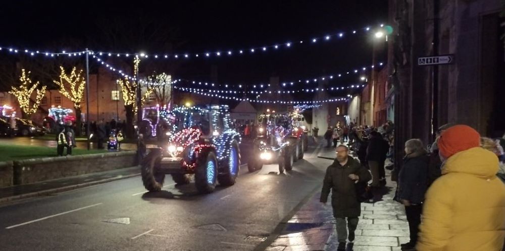 lit up decorated tractor in a line of tractors In Broad Street with crowds watching