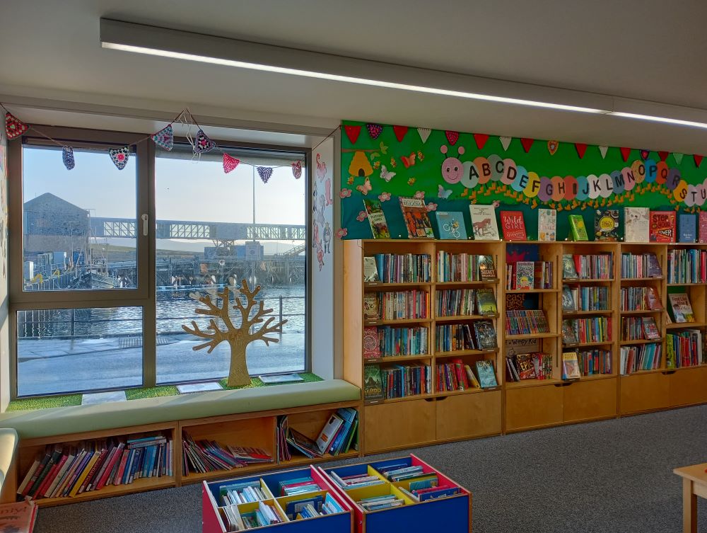 shelves of books for young people and a large window with a view over the harbour