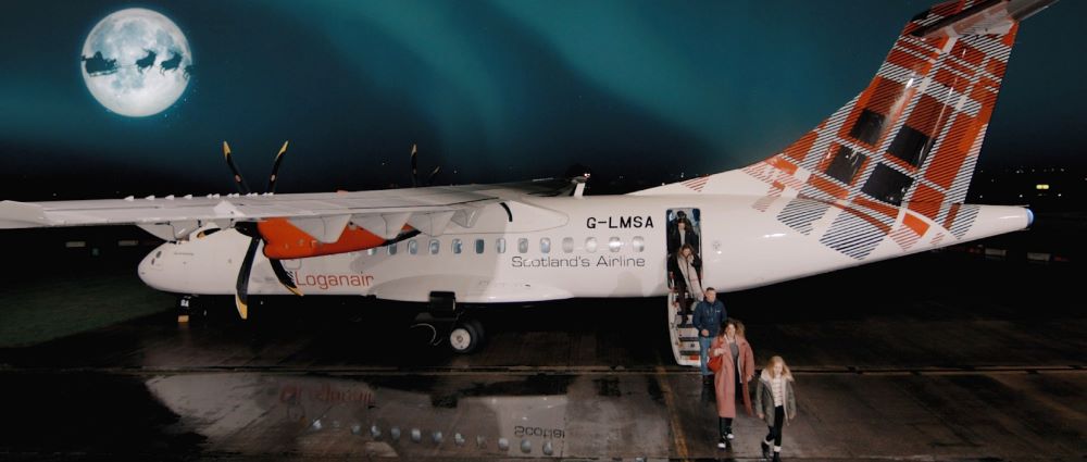 people leaving down the steps from a Loganair plan in the sky is a full moon with the silhouette of Santa and his reindeer flying across the sky