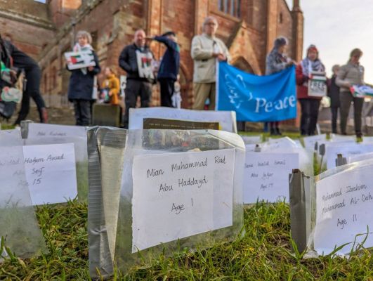the names of young children killed in Gaza and behind some of those at the vigil with a Peace Banner