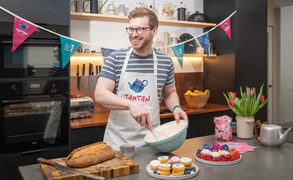 Dr James Morton smiling as he mixes some dough, in front of him is a selection of bread and cakes