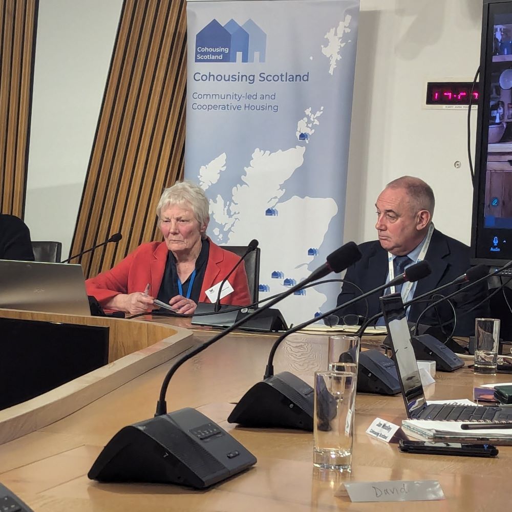 Jenny and the Housing Minister sitting round the desks in the Scottish Parliament