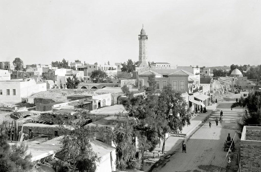 a busy streets with trees and low buildings a tall minaret dominates the area