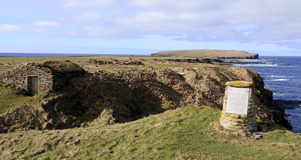 the fishermen's hut at Birsay with the brough in the background. the boat nousts surround the hut