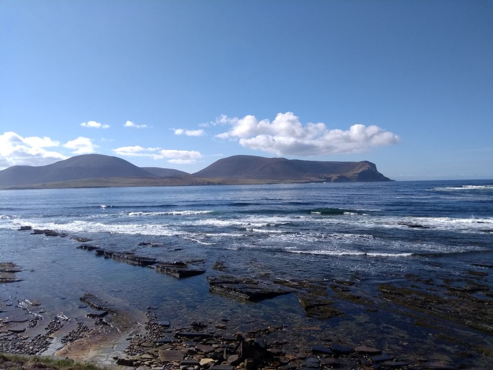 the hills of Hoy on a sunny day from Warebeth with the exposed flat stones of the shore