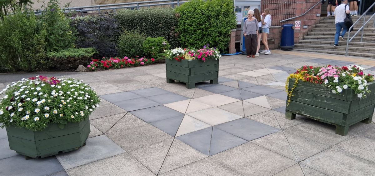 three planters filled with flowers at the paved entrance