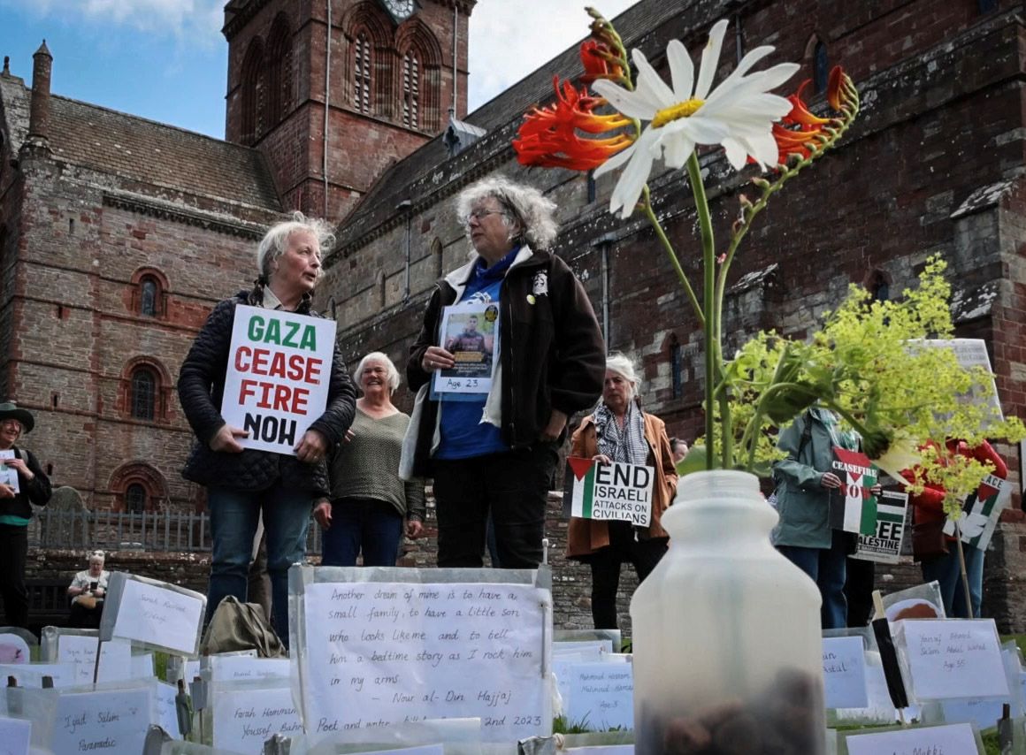 flowers at the memorial to those killed in Gaza with two women standing in vigil holding posters