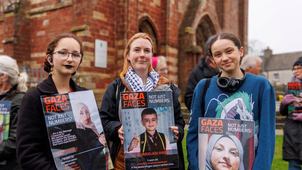 three women with posters bearing the images of people killed in Gaza