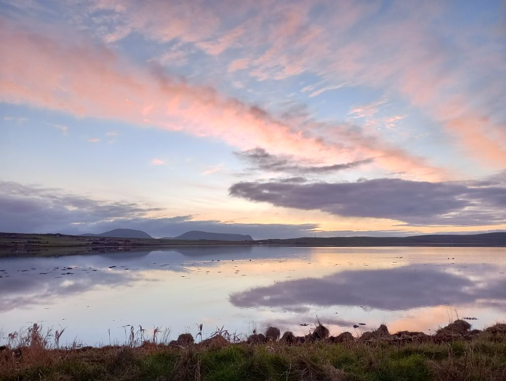 an evening sunset over a very still Stenness Loch with the hills of Hoy in the far distance