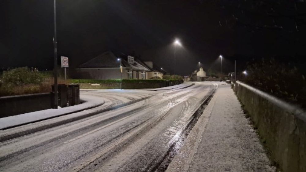 a lightly covered snowy street in Kirkwall with houses on one side, a single street lamp at the dark of night