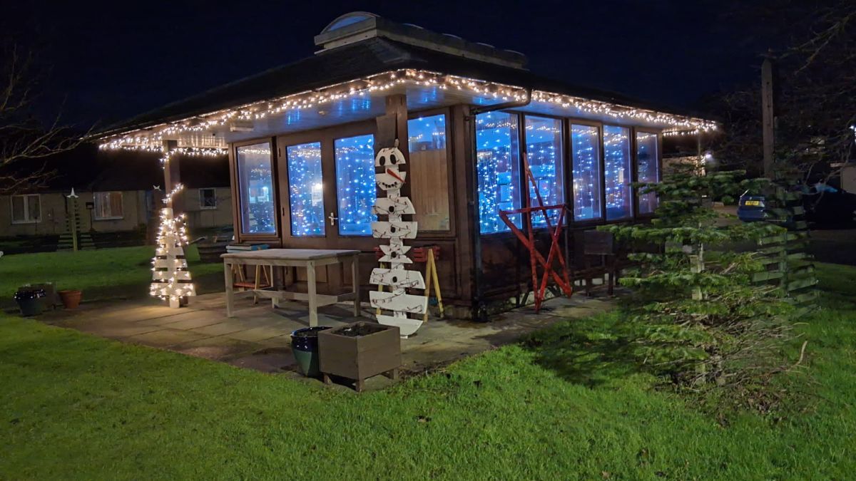 a wooden garden house decorated filled with Christmas lights and on either side of its porch pallet made tree and snowman