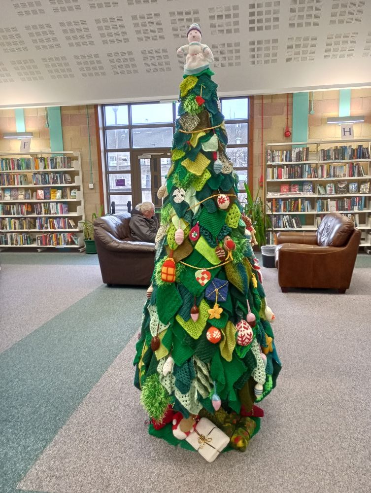 a knitted Christmas tree in Orkney Library surrounded by book shelves and seats