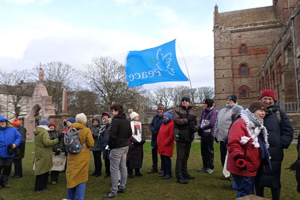 a gathering of people on the Kirk Green with a large Peace flag