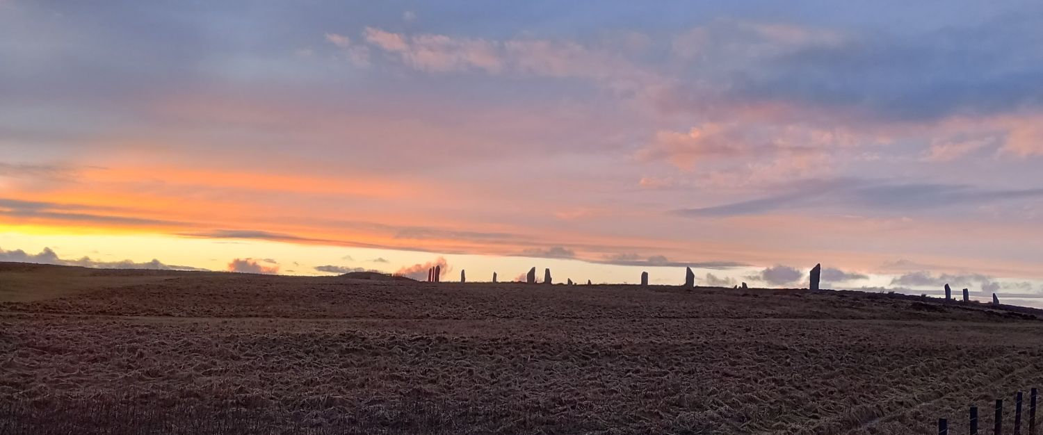 a pale red and golden setting sun over the Ring of Brodgar