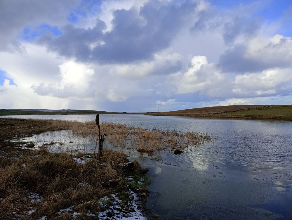a still loch in Sandwick with a rusted metal object sticking out